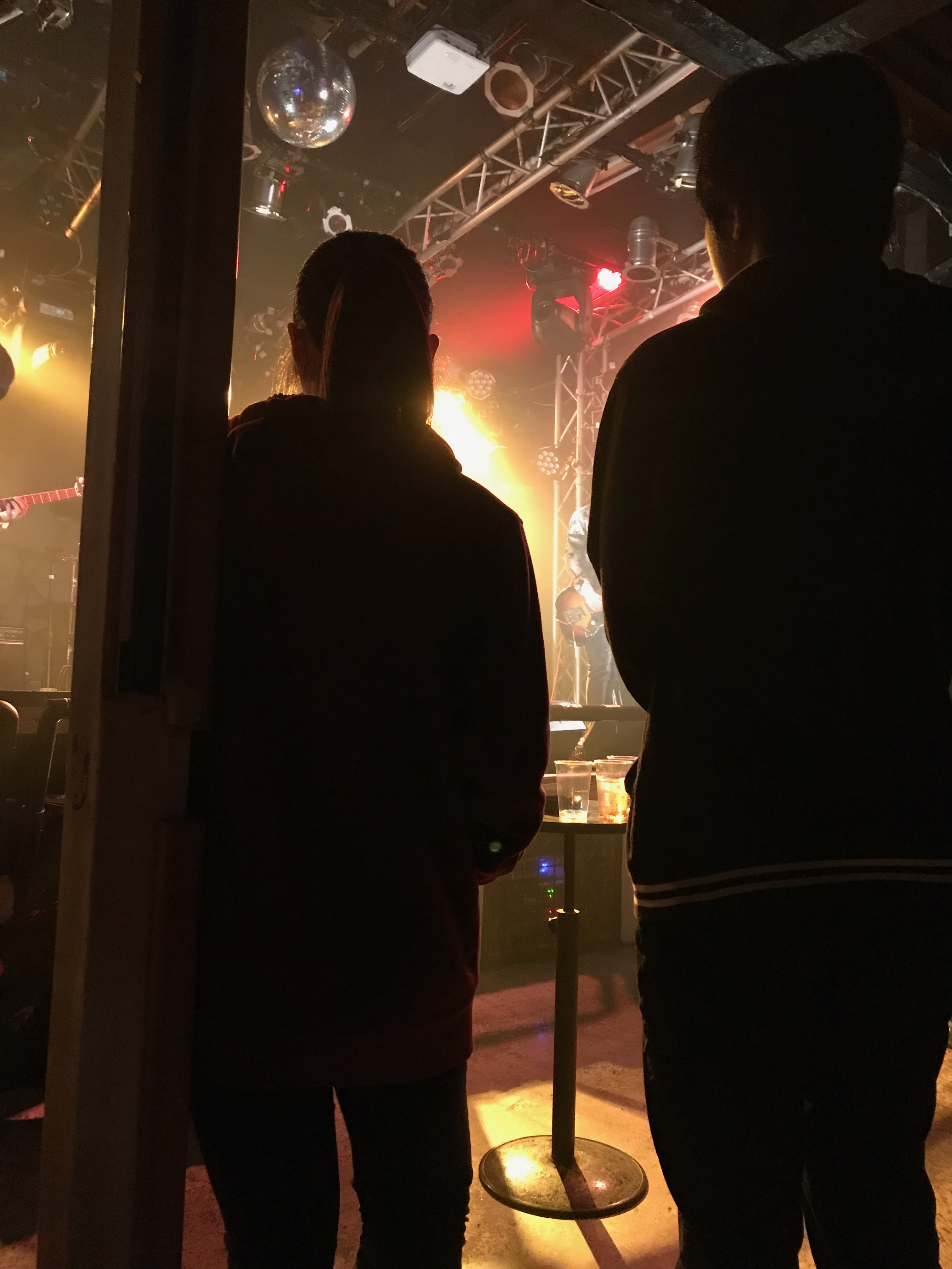 ライトアップされたステージ、アーティストのパフォーマンスを見る学院生２人の後ろ姿。